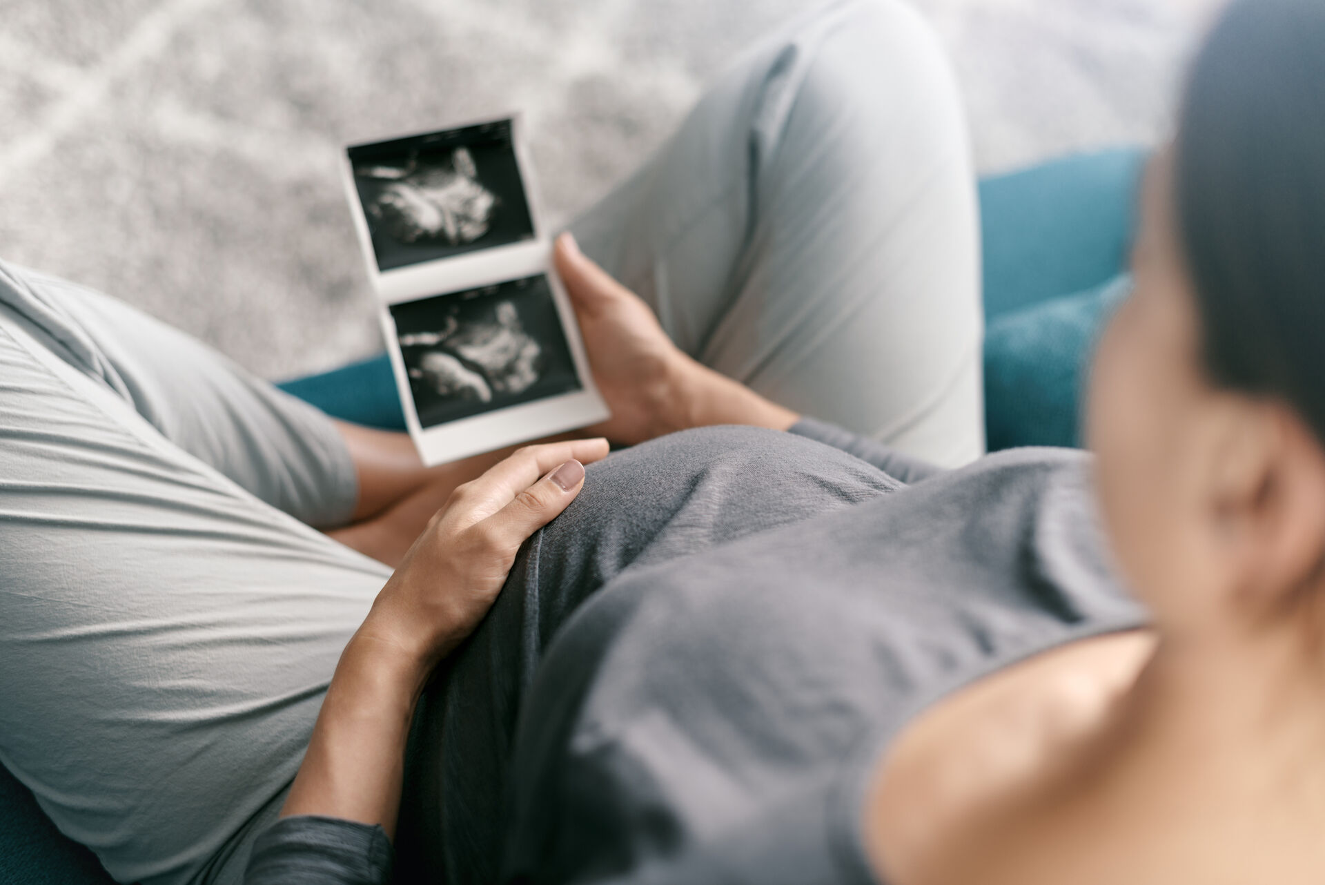 Eine schwangere Frau sitzt entspannt und blickt auf ein Ultraschallbild. Sie hält sanft ihren Bauch und scheint sich auf das bevorstehende Baby zu freuen. Die Atmosphäre ist ruhig und intim.