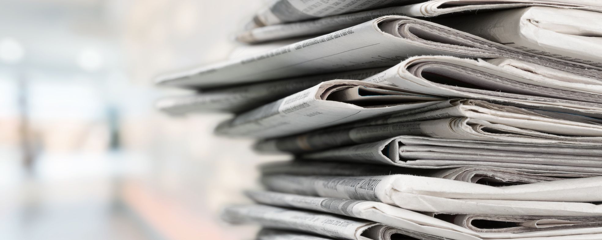 Ein Stapel gefalteter Zeitungen, die übereinander gestapelt sind. Der Hintergrund ist unscharf, was den Fokus auf die Zeitungen verstärkt. Die Zeitungen sind in verschiedenen Grüntönen gehalten und vermitteln den Eindruck von Information und Neuigkeiten.