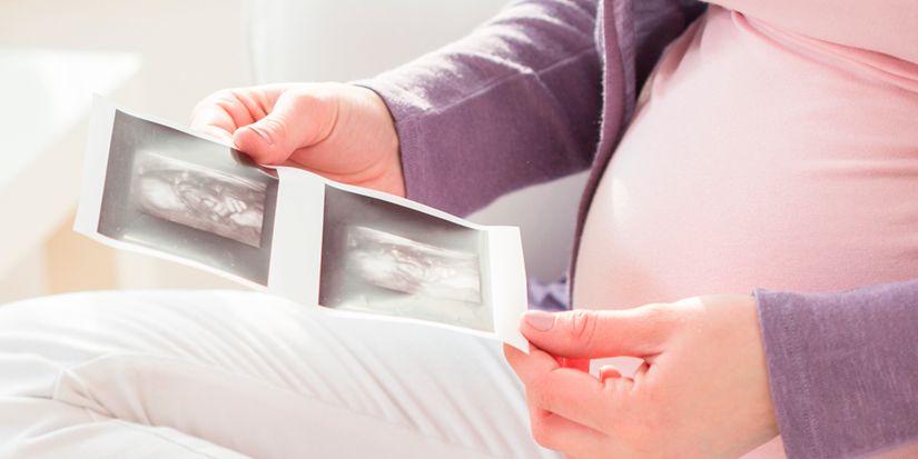 A pregnant person holds two ultrasound images, showcasing the developing baby. The focus is on the images, with the individual's belly slightly visible in the background, highlighting the joy and anticipation of pregnancy.
