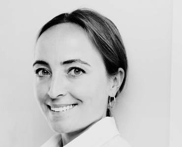 A smiling woman with long hair, wearing a light shirt and hoop earrings, poses against a light background. Her expression conveys warmth and approachability.