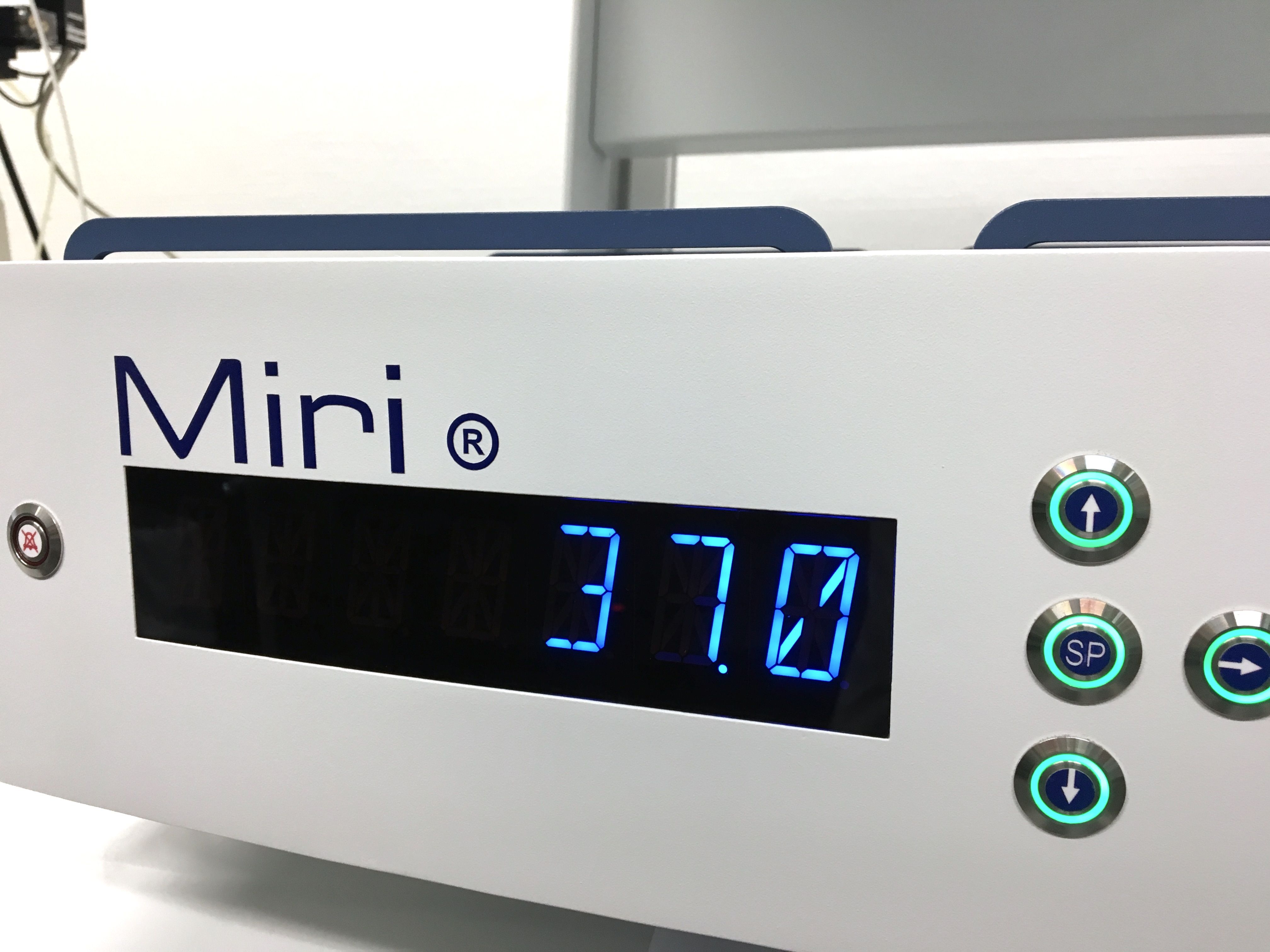 The image features a device labeled "Miri" with a digital display showing the number "37.0." There are several buttons on the front, indicating settings or controls. The overall design is sleek and modern, primarily in white and blue colors.